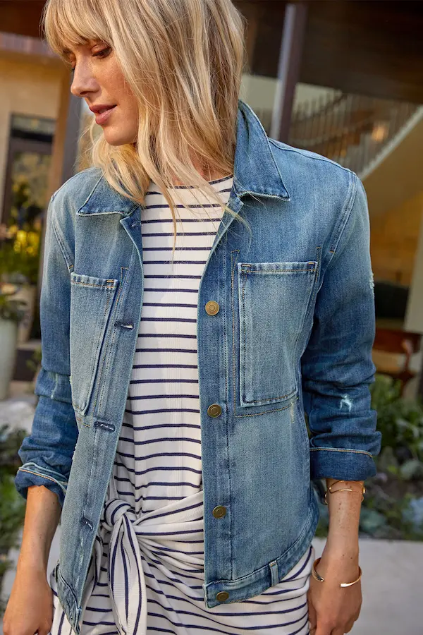 Best denim jacket - A woman wearing a denim jacket with a striped shirt, standing outside. Perfectly styled jean jacket for any occasion.