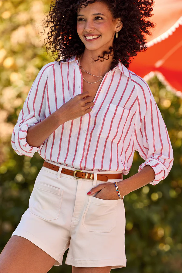 ways to wear white jeans: A woman in a navy vest and white jeans, standing by a vintage convertible, demonstrating a modern layered look with white denim.