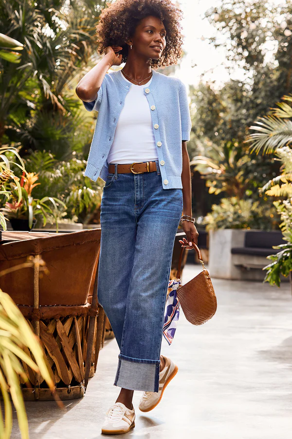 Spring 2025 trends highlighted in a powder blue short-sleeve cardigan paired with classic denim and leather accessories, perfect for transitional weather