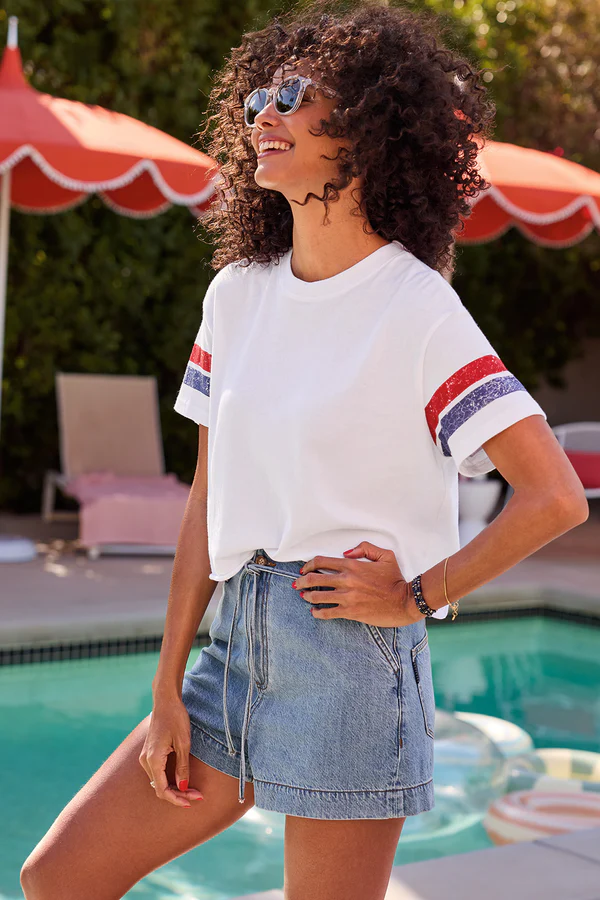 summer outfit ideas: A woman relaxing poolside in a blue striped sweater, white shorts, and a baseball cap, perfect for a laid-back summer weekend.